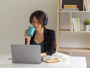 Retrato da empresária que trabalha em casa, usando laptop, fone de ouvido e bebendo café na sala do escritório em casa