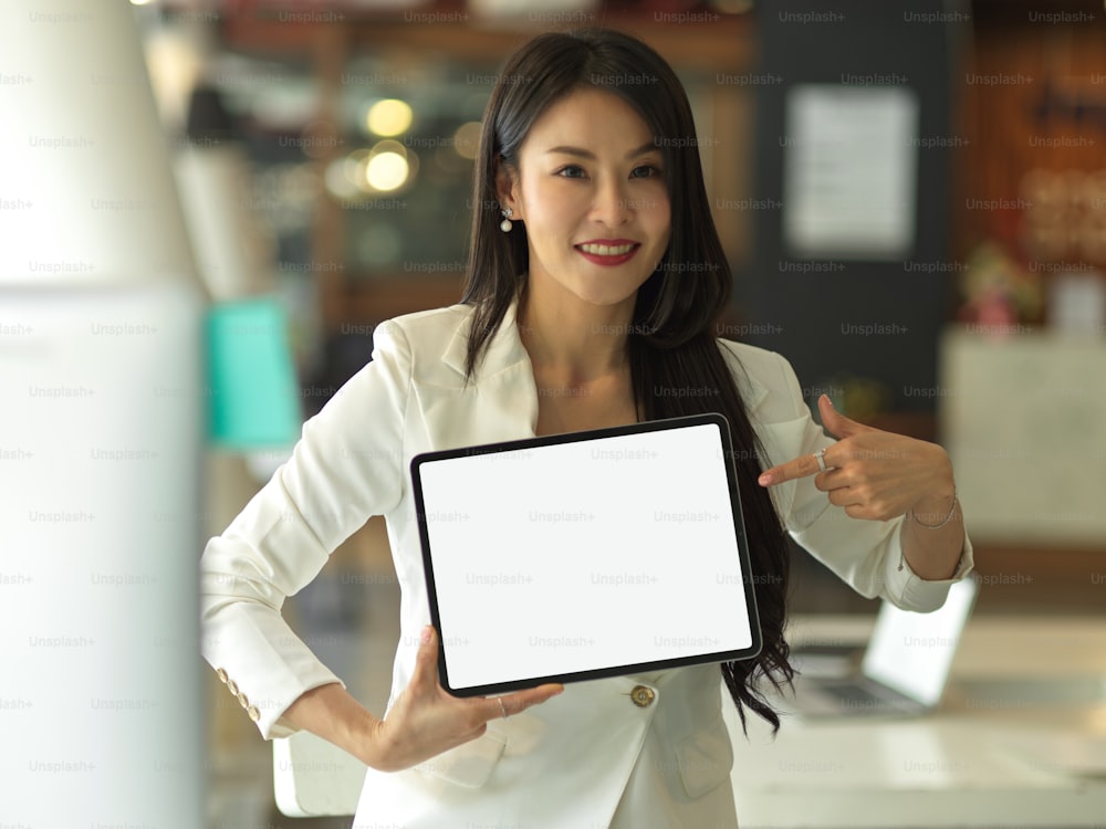 Porträt einer Geschäftsfrau im weißen Anzug präsentiert digitales Tablet mit Mock-up-Bildschirm zur Kamera, Clip-Pfad