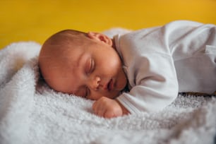 Adorable baby sleeping on a white furry blanket on a yellow sofa at home