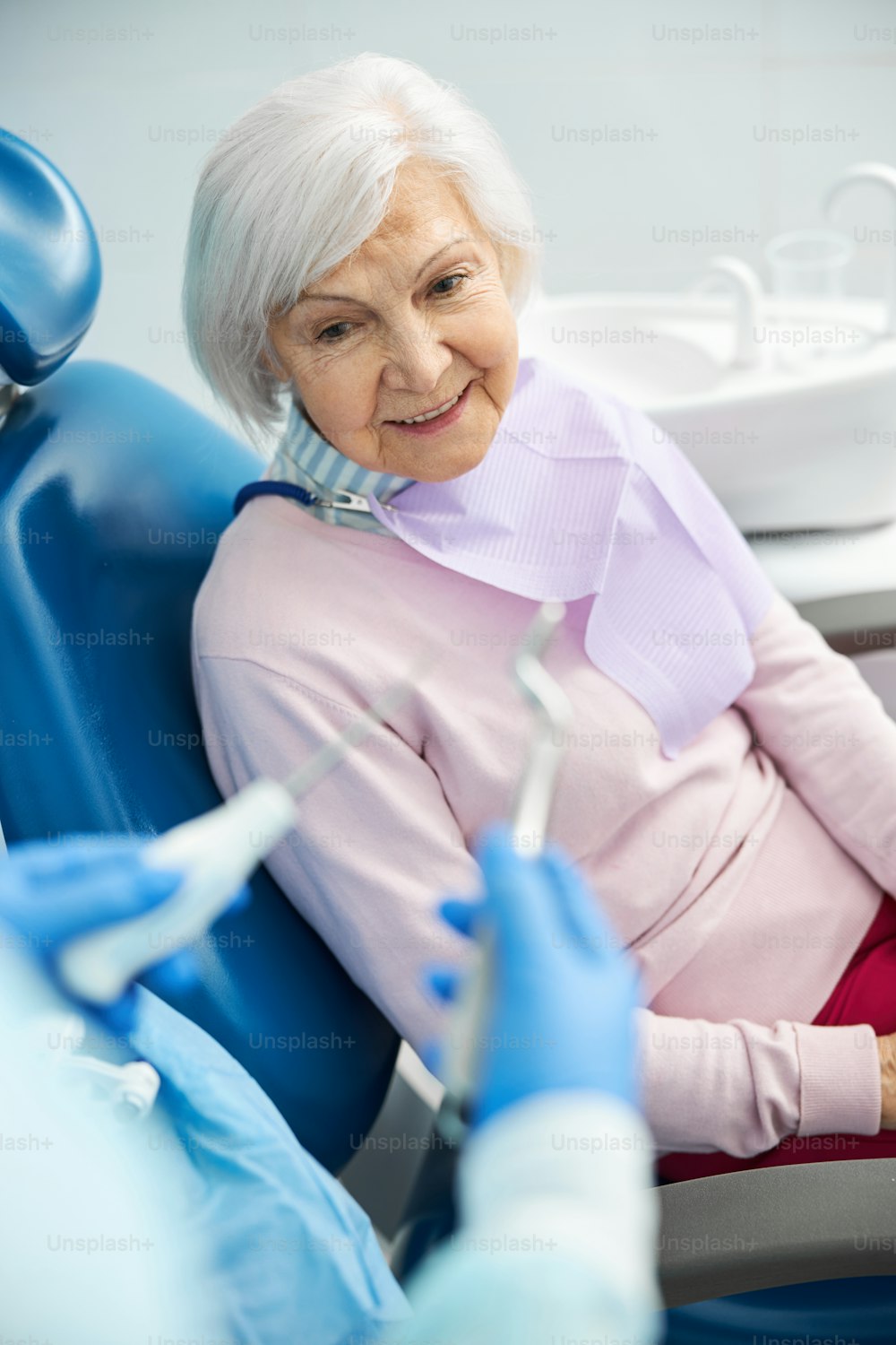 Aging female waiting in a dental chair for a stomatologist with extracting forceps and elevator