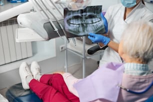 Presentation of teeth radiograph to a female pensioner, lying on dental chair and listening to dentist