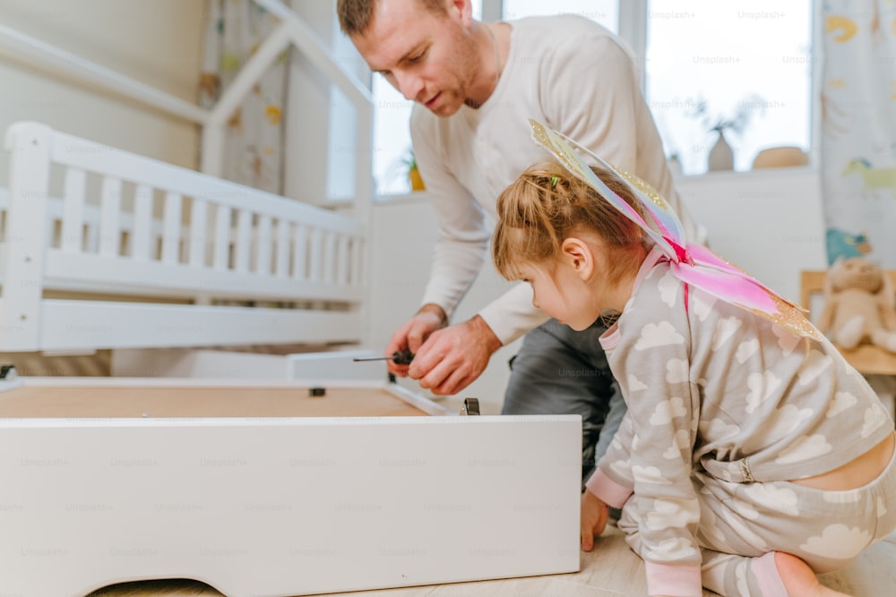 La niña de 4 años ayuda a su padre a armar o arreglar el cajón de la cama en el dormitorio de los niños.