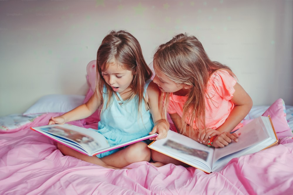Happy Caucasian sisters girls reading books in bedroom. Children siblings at home spending time together. Kids education development learning. Real people authentic lifestyle.
