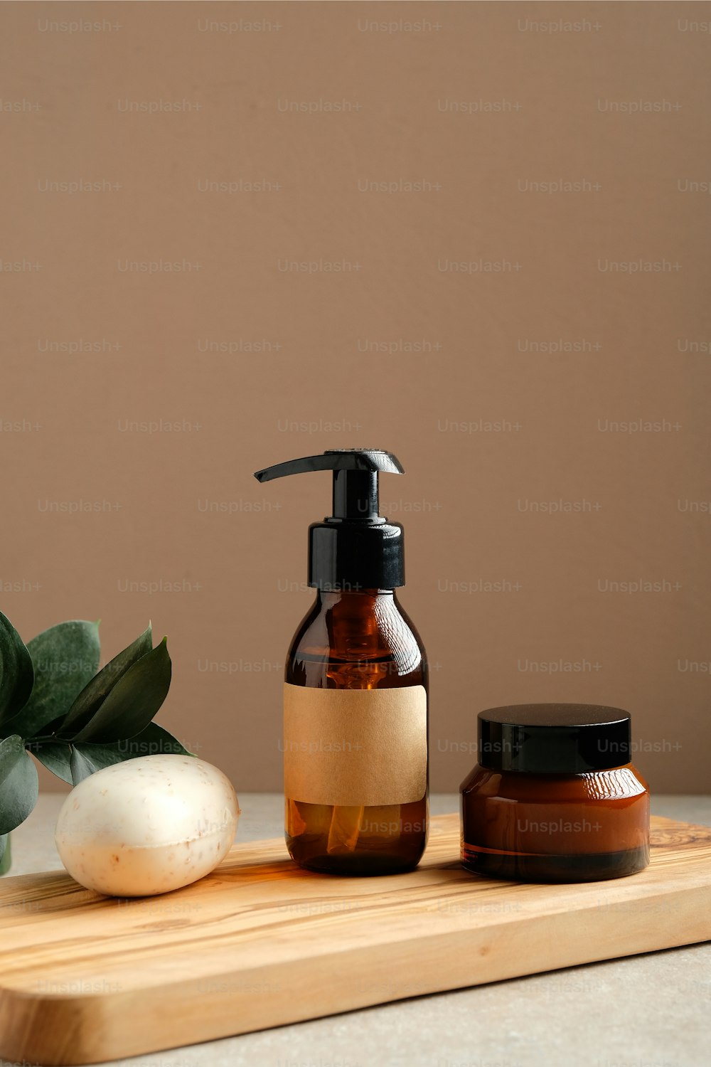 Organic natural cosmetic products with green leaves on wooden board. Amber glass dispenser bottle, body cream jar, homemade soap. Bathroom SPA beauty products packaging design.