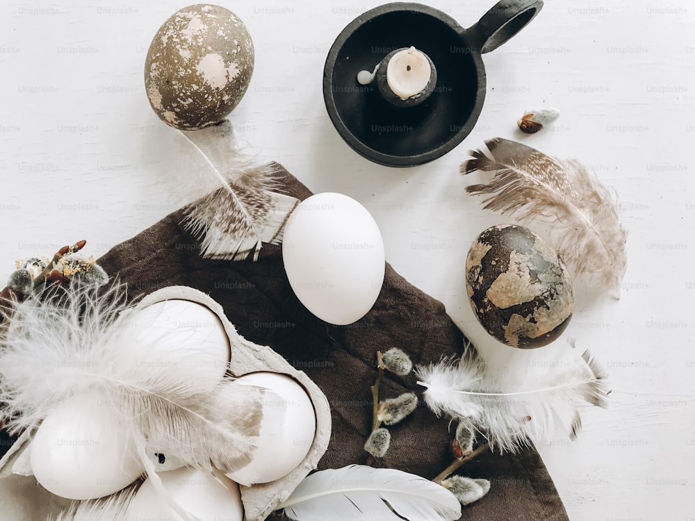 Huevos de pascua naturales, plumas, ramas de sauce, vela sobre tela rústica sobre mesa blanca envejecida. Piso de Pascua. Elegante bodegón rural. Est�ética moderna y sencilla, colores blanco y gris