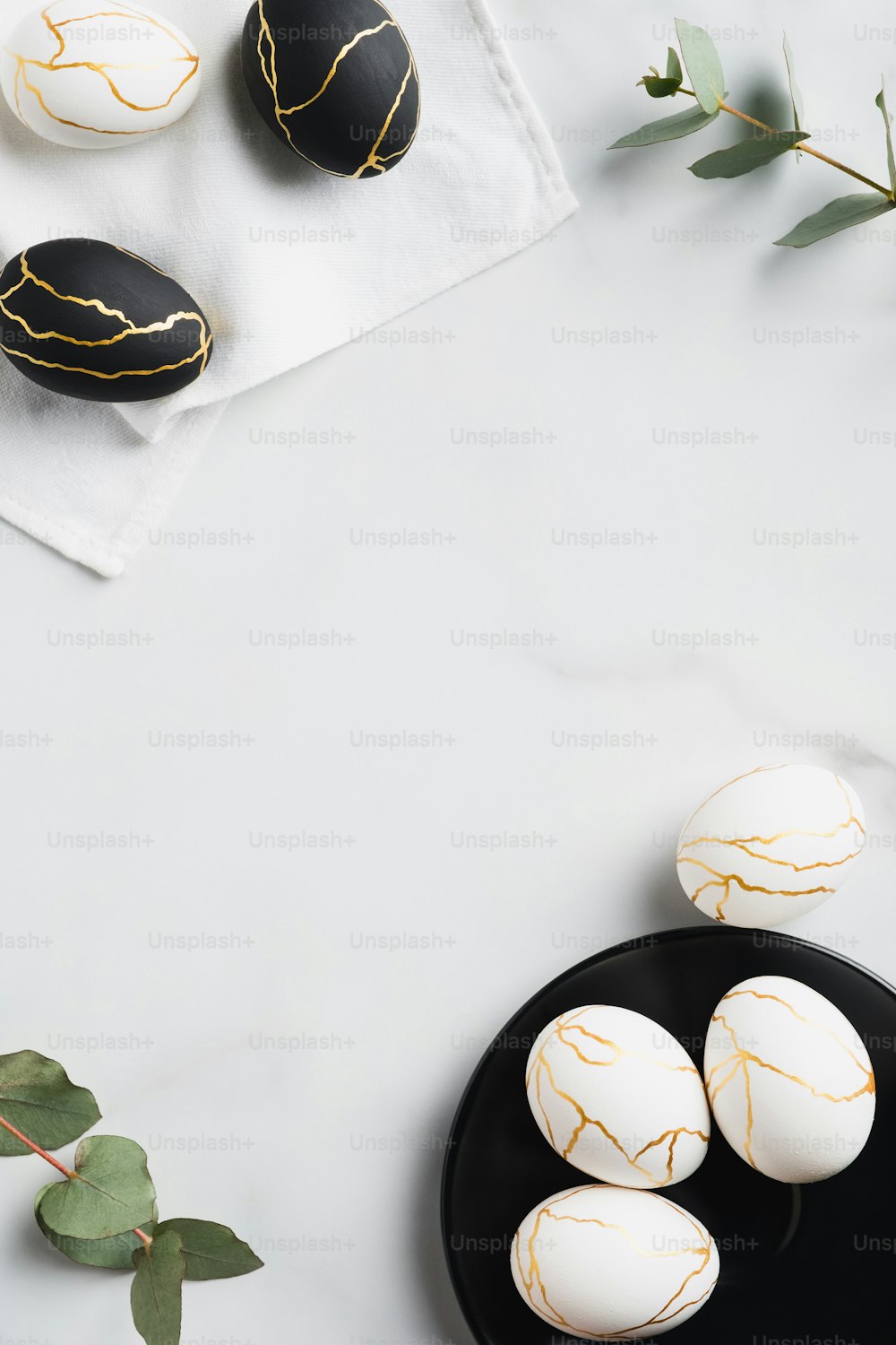 Frame of white and black Easter eggs decorated gold and eucalyptus leaves on marble table. Flat lay, top view. Happy Easter vertical banner design.
