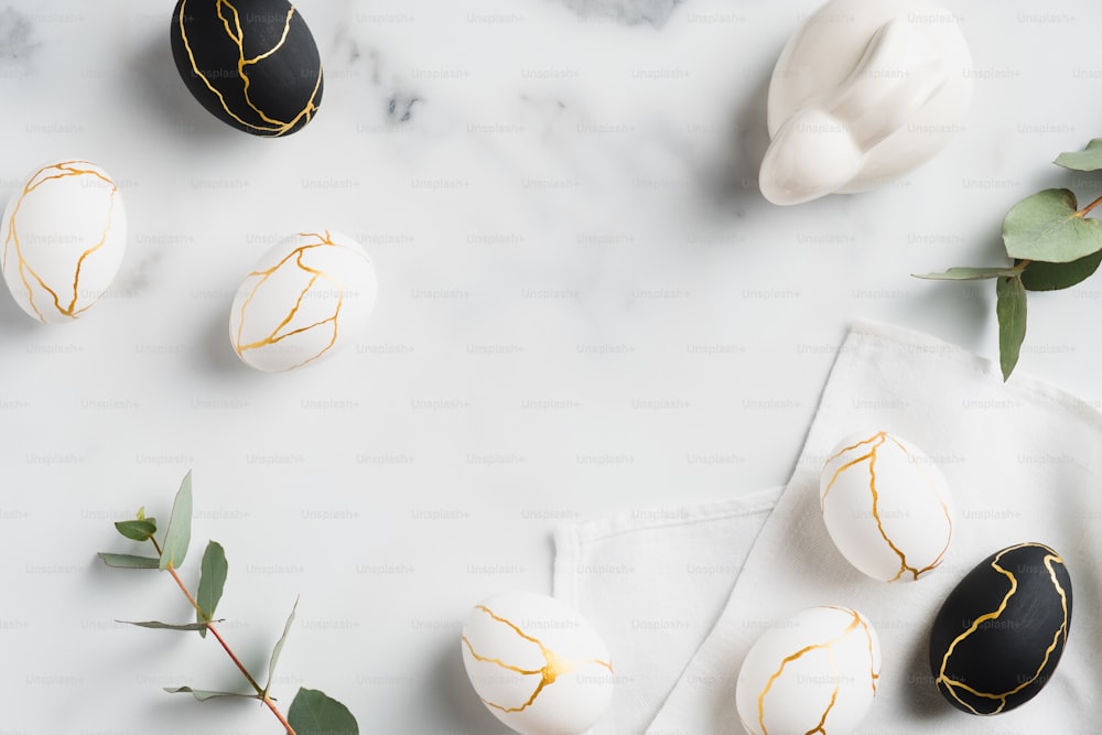 Easter flat lay composition. Easter bunny, luxury white and black Easter eggs decorated gold and eucalyptus leaves on marble table. Flat lay, top view