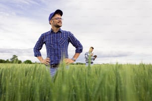 Portrait of farmer standing in green wheat field with his colleague in background.