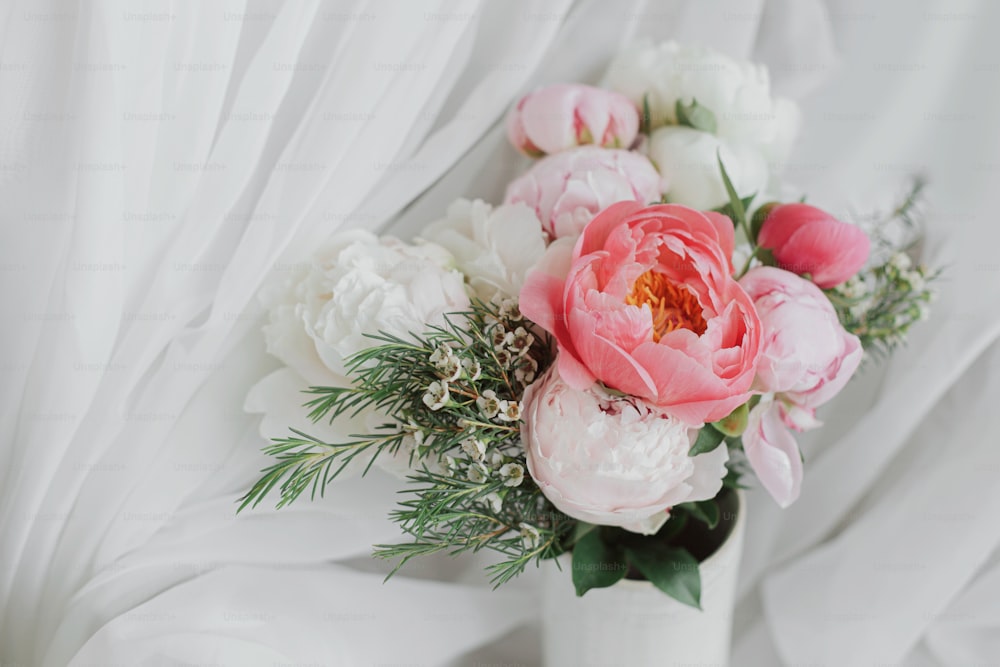 Schöne stilvolle Pfingstrosen Bouquet auf dem Hintergrund aus weichem weißem Stoff. Rosa und weiße Pfingstrosenblüten in Keramikvase auf pastellfarbenem rustikalem Hintergrund. Alles Gute zum Muttertag. Moderner Brautstrauß