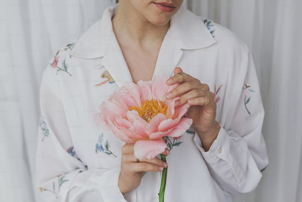 Sensual beautiful woman with pink peony in hands. Young stylish female in boho floral shirt gently holding big peony flower. Tender soft image. Spring aesthetics