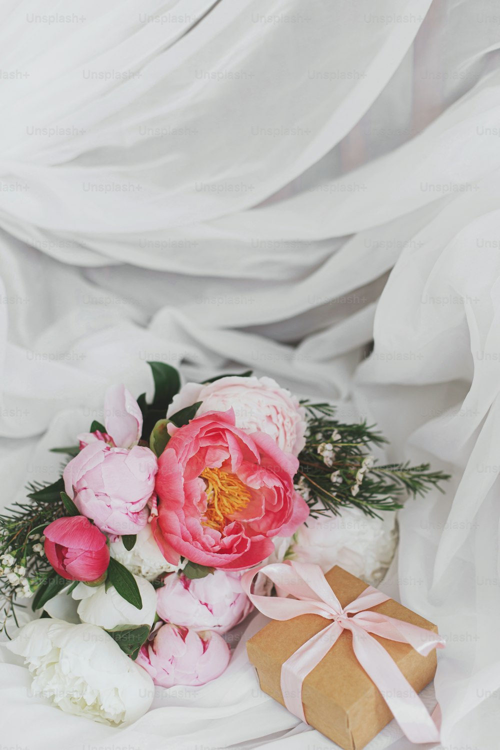 Bellissimo bouquet di peonie alla moda e confezione regalo su morbido tessuto bianco su sedia rustica. Fiori di peonia rosa e bianca e presente. Buona festa della mamma. Mattina nuziale