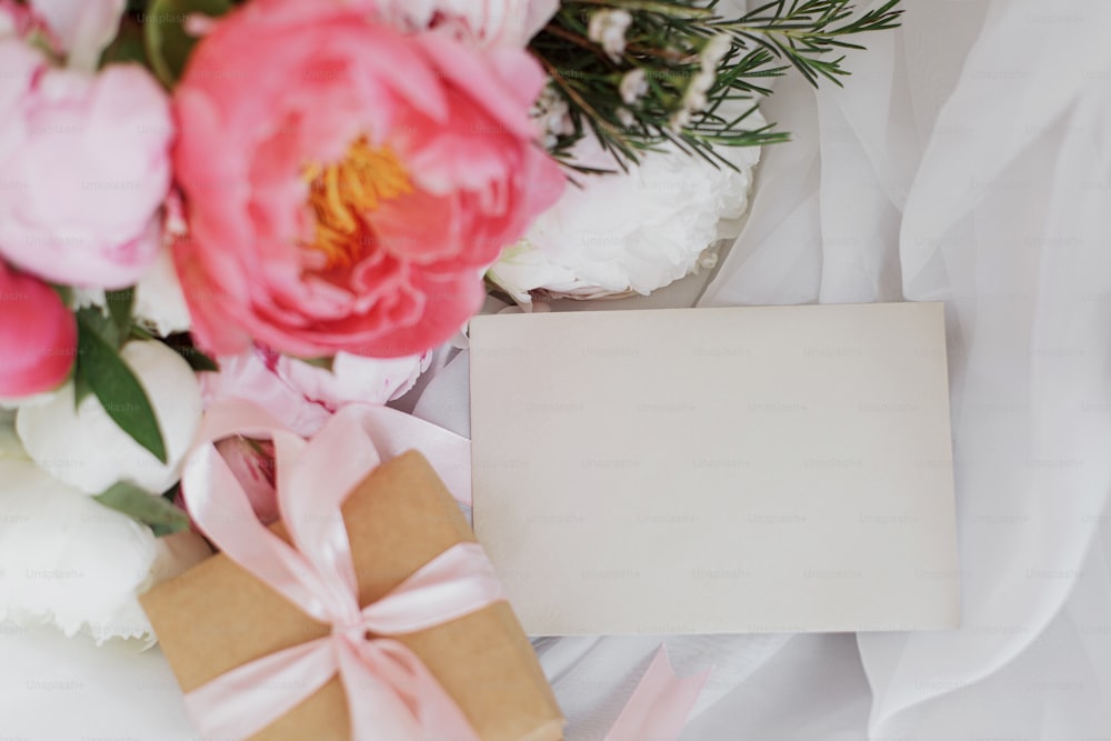 세련된 인사말 카드, 아름다운 모란 꽃다발, 소박한 의자에 부드러운 흰색 천에 선물 상자. 분홍색과 흰색 모란 꽃, 선물, 엽서. 텍스트를 위한 공간입니다. 해피 어머니의 날