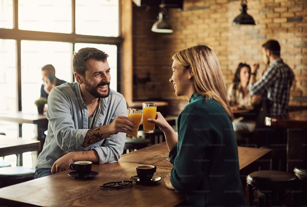 Uomo felice e la sua ragazza che brindano con succo d'arancia in un pub.