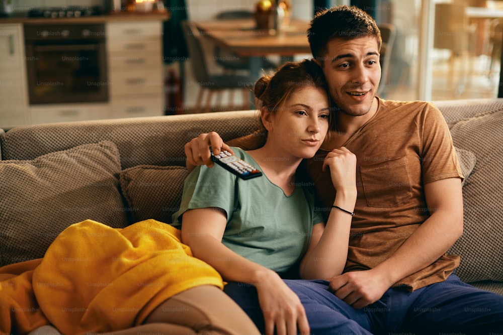 自宅のソファーでくつろぎながらテレビを見ている笑顔のカップル。