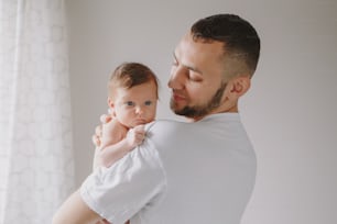 Young Caucasian bearded dad carrying newborn baby on shoulder. Male man parent  holding child daughter son in arms. Authentic family lifestyle documentary moment. Fathers Day holiday.