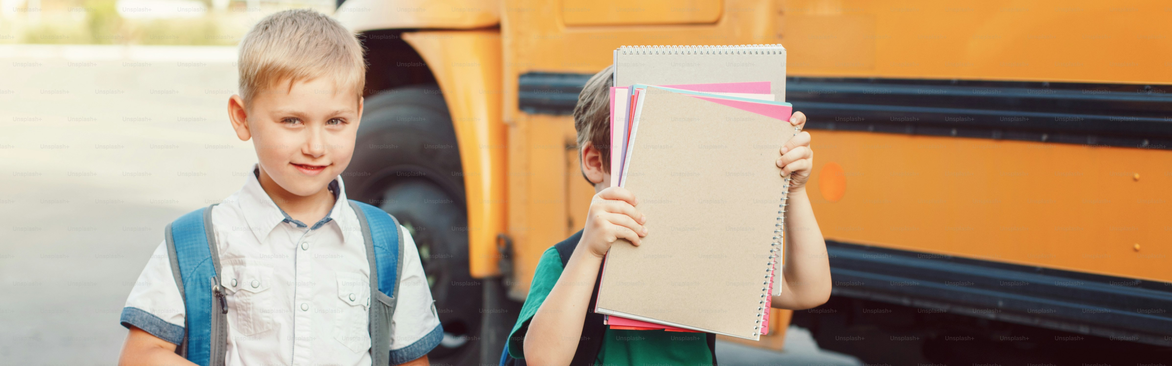 Dos divertidos niños caucásicos felices, estudiantes, niños parados junto al autobús amarillo el día 1 de septiembre. Educación y concepto de vuelta al cole. Niños dispuestos a aprender, a estudiar. Encabezado de banner web para sitio web.