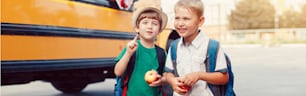 Zwei lustige glückliche kaukasische Jungen Studenten Kinder mit Äpfeln stehen am gelben Bus am 1. Septembertag. Bildung zurück in die Schule. Kinder, die bereit sind zu lernen und zu lernen. Webbanner-Header für Website.