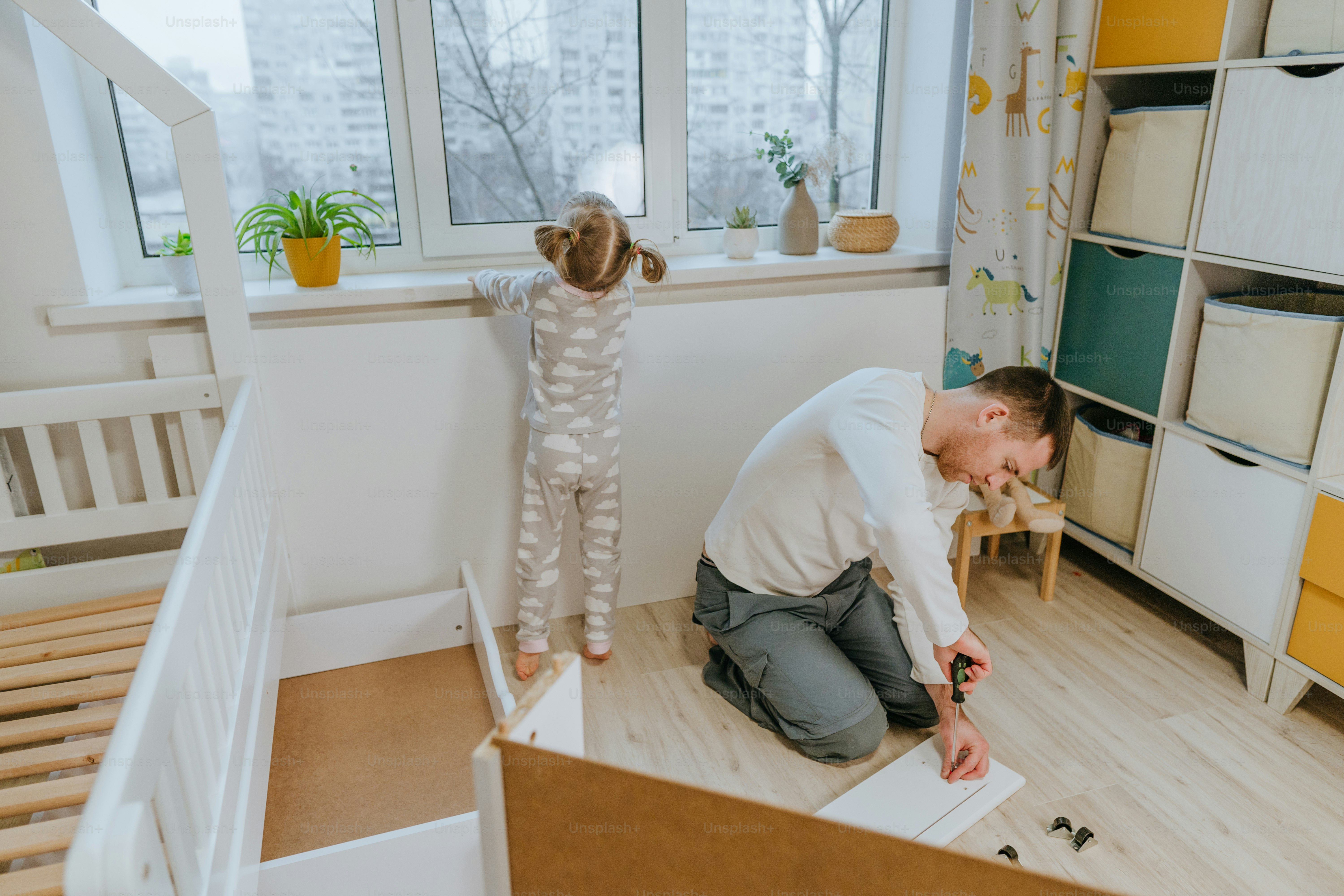 Little 4-years girl helps her father assemble or fixing the drawer of bed in the kids bedroom.