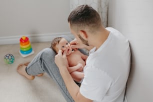 Happy Caucasian father holding newborn baby on laps knees. Man parent embracing rocking child daughter son. Authentic lifestyle candid moment. Proud young dad. Family fathers day.