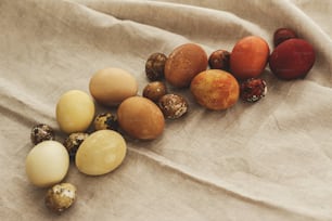 Uova di Pasqua moderne ombre su sfondo rustico in tela di lino con spazio per il testo. Buona Pasqua! Uova tinte al naturale nei colori marrone, giallo e rosso sfumate su tessuto grigio. Estetico