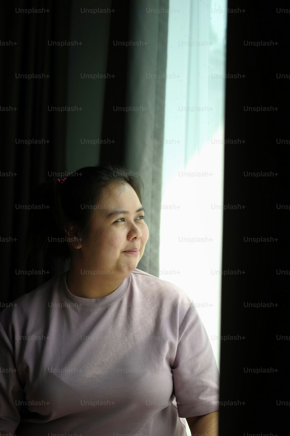 Porträt einer fettleibigen Frau, die lächelt und wegschaut, während sie in der Nähe des Fensters steht.