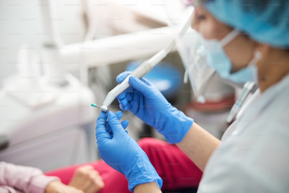 洗浄処置の前に歯科用ハンドピースの頭部にある青いプロフィーカップの位置を調整する女性歯科医