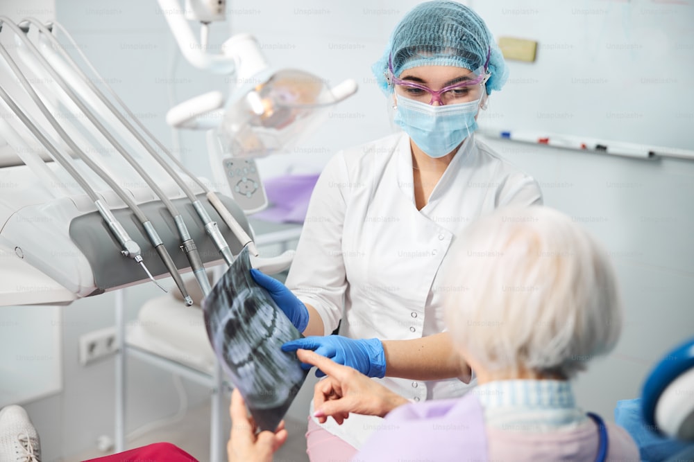 Professionista dentale che condivide informazioni sulla malattia dentale del paziente puntando il dito sulla pellicola radiografica dei denti