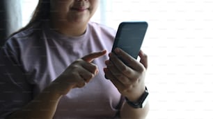 Foto recortada de una mujer gordita feliz usando un teléfono inteligente en casa.