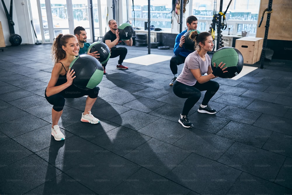 Smiling attractive young Caucasian woman working out with the group of sportspeople at the gym