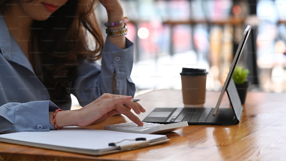 Copped shot of female accountant  hand holding pen working with computer tablet and calculate business data.