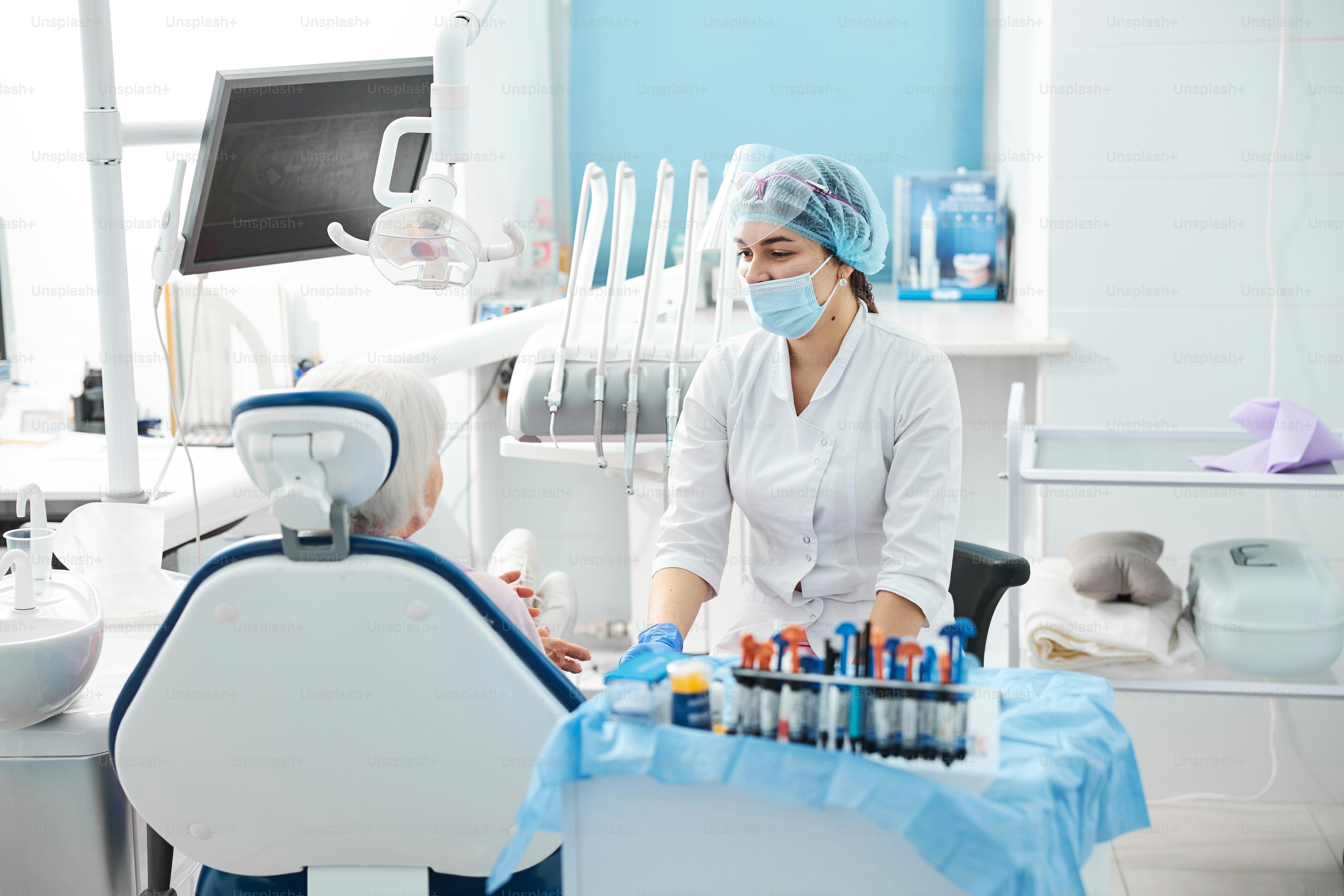 Zahnarzt legt Hände auf einen medizinischen Tisch mit Kompositharzen und Werkzeugen und tauscht Blicke mit dem Patienten aus