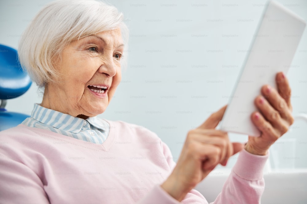 Grey-haired woman learning the usage of modern tablet before her face and pushing her finger into screen