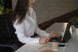 Side view of young female office worker smiling and working with computer tablet at office desk.