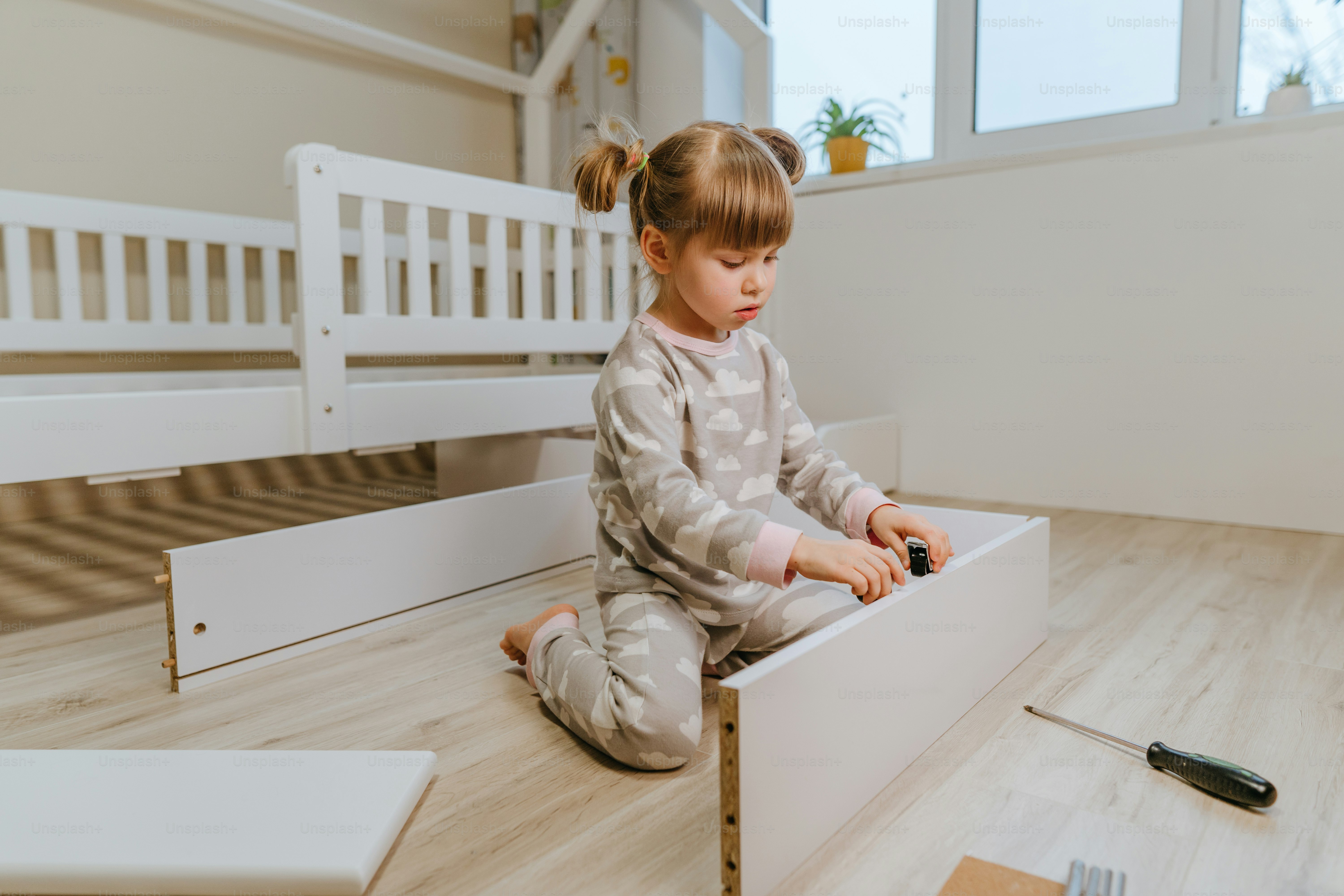 Little 4-years girl assemble the drawer of bed in the kids bedroom.