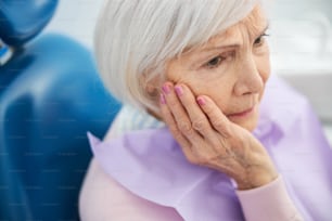 Depressed pensioner feeling pain in her mouth and holding her hand on a cheek while looking away