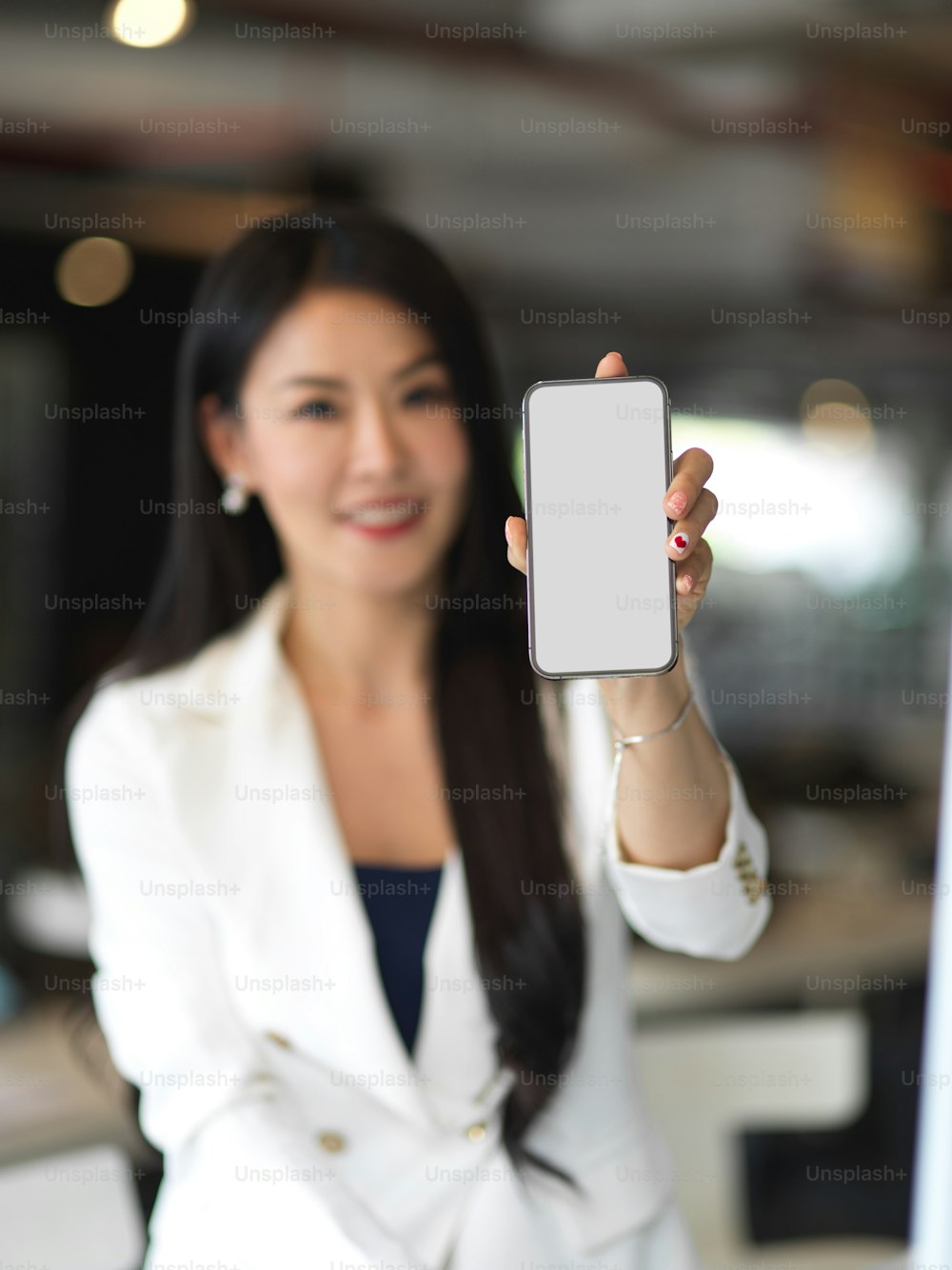 Porträt einer Geschäftsfrau, die Smartphone mit Mock-up-Bildschirm zur Kamera im verschwommenen Hintergrund zeigt, Clip-Pfad