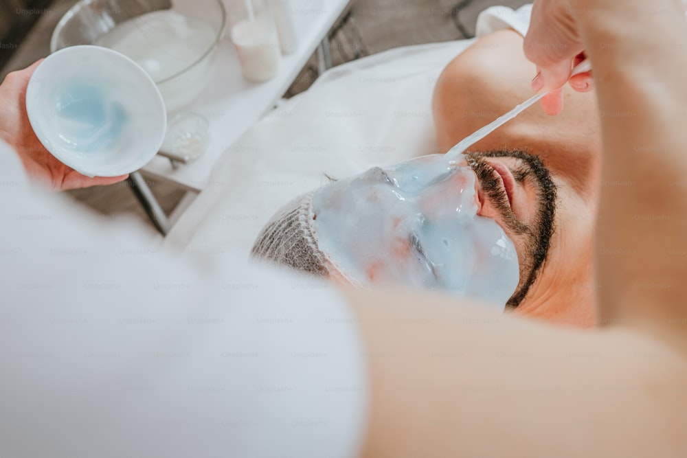Esteticista fazendo procedimento de limpeza facial usando máscara de algas para um homem no salão de beleza