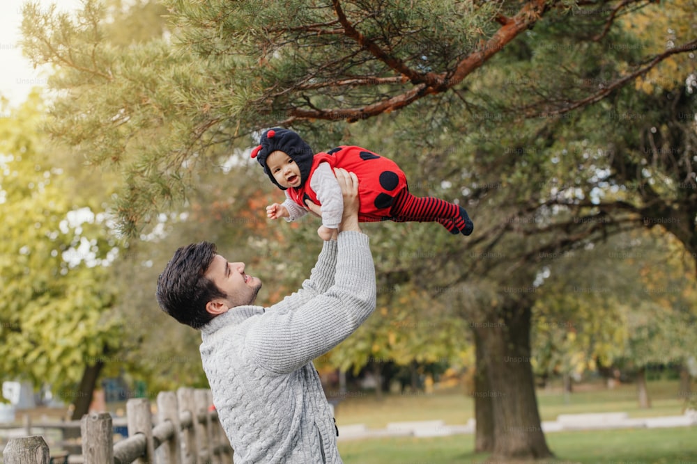 Happy smiling Caucasian father dad with cute adorable baby girl in ladybug costume. Family in autumn fall park outdoor. Halloween holiday seasonal concept.