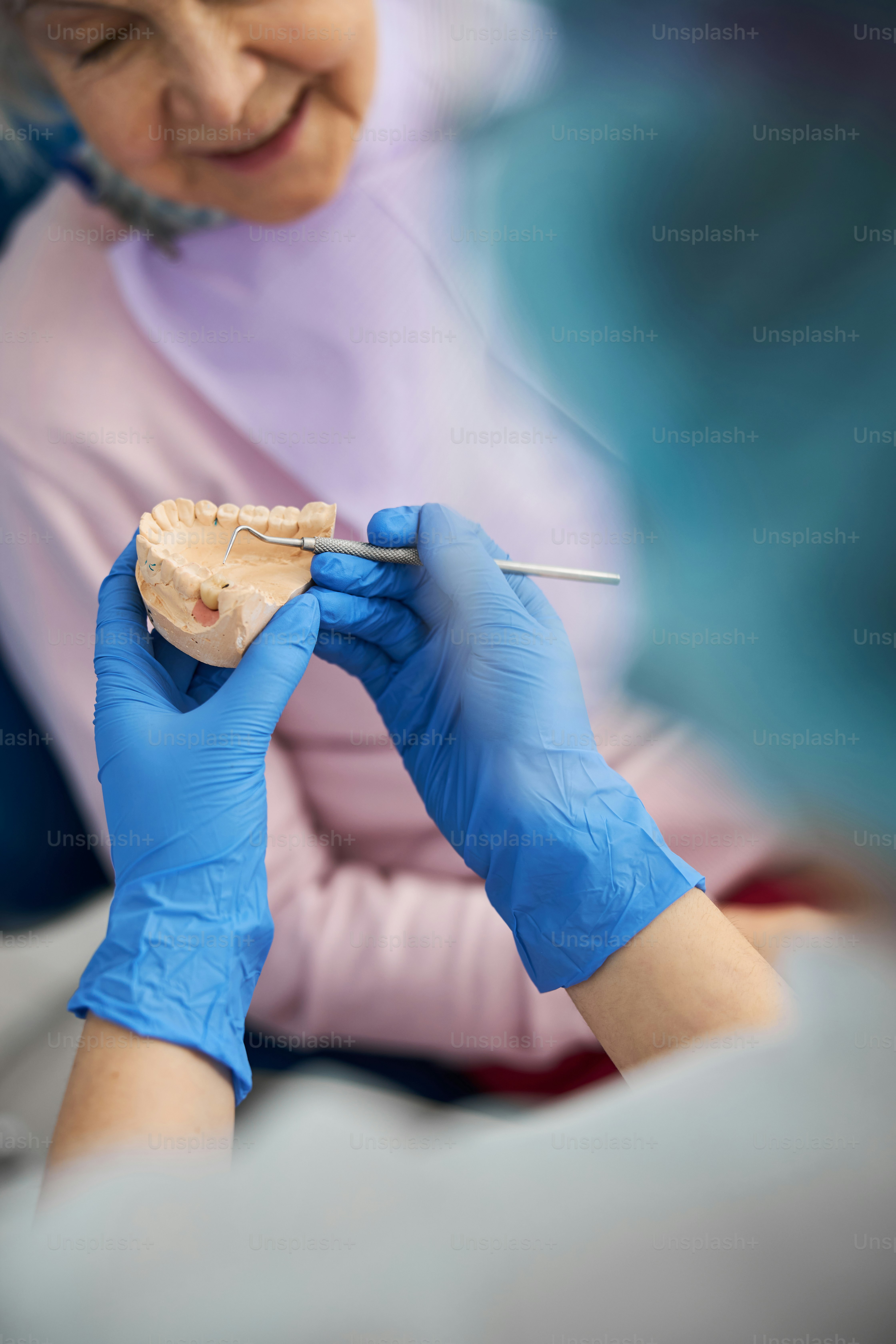 Adulte tenant une sonde dentaire et frappant avec sa pointe sur le moule moulé de la mâchoire près d’une femme âgée