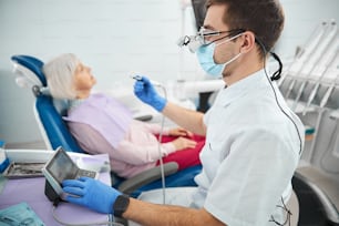Trabajador de una clínica dental con guantes médicos azules y máscara operando una unidad de control para la pieza de mano cerca de un paciente