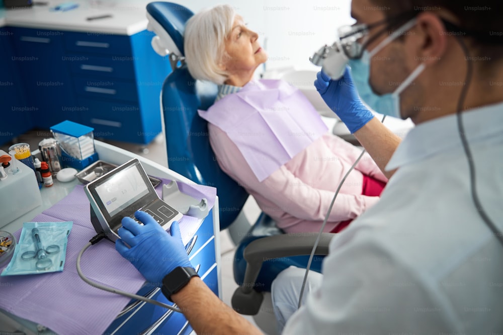 Homme en blouse médicale plaçant sa main gauche sur le contrôleur de foret dentaire et saisissant des données tout en tenant la pièce à main