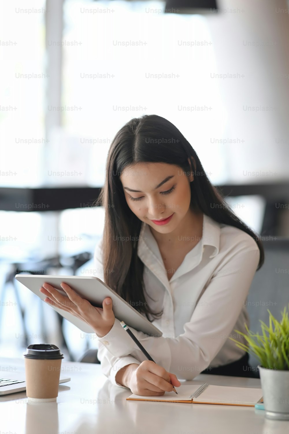 Retrato de una joven empresaria usando una tableta digital y tomando notas en un cuaderno de notas.