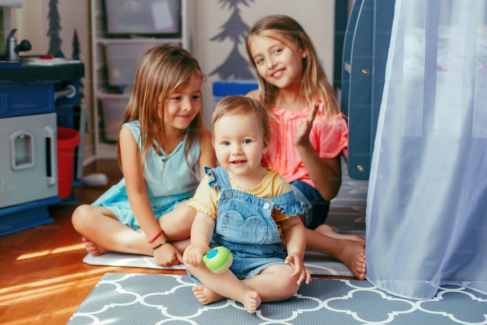 Caucasian girls siblings sitting on floor at home and playing with sister toddler. Happy friends relationship concept. Adorable children playing together. Authentic candid lifestyle moment.