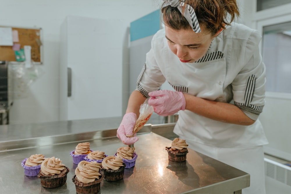 製菓スタジオでクリームと新鮮なベリーでカップケーキを作るピンクの手袋をはめた女性菓子職人の接写