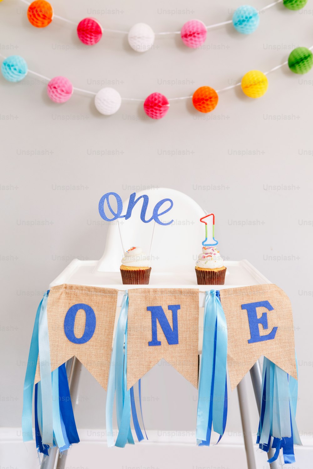 Festive background decoration for birthday celebration. Letters text one and one candle in small cupcakes for baby child birthday. Garland decoration on background. Cake smash first year.