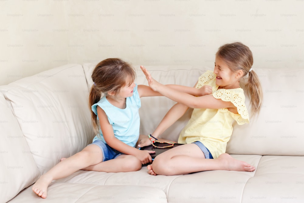Two little mad angry girls sisters having fight at home. Friends girls can not share gadget tablet. Lifestyle authentic funny family moment of siblings quarrel life. Kids bad behaviour.