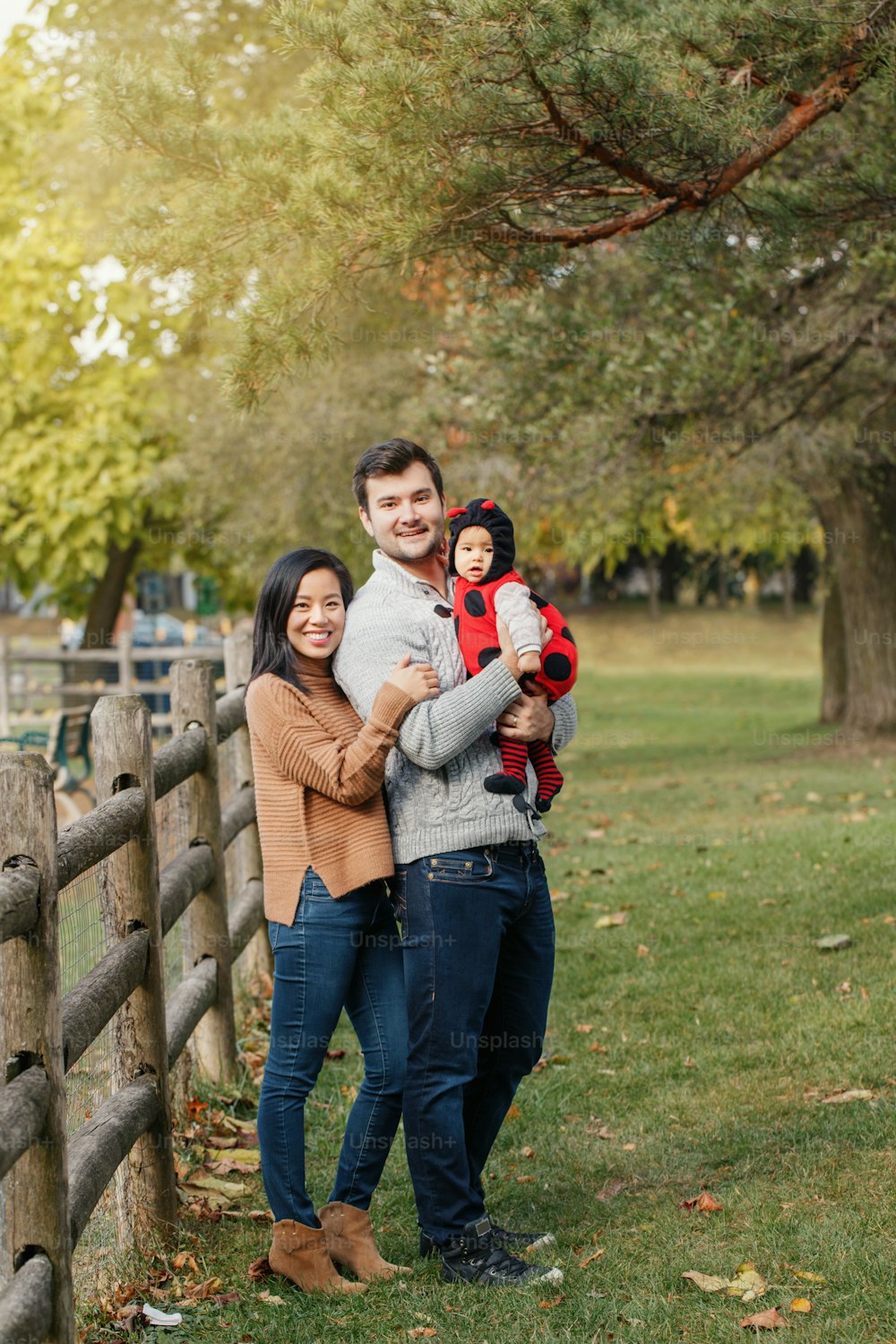 Happy Halloween. Smiling Asian Chinese mother and Caucasian father dad with baby girl in ladybug Halloween costume. Ethnic family in autumn fall park outdoor celebrating holiday.