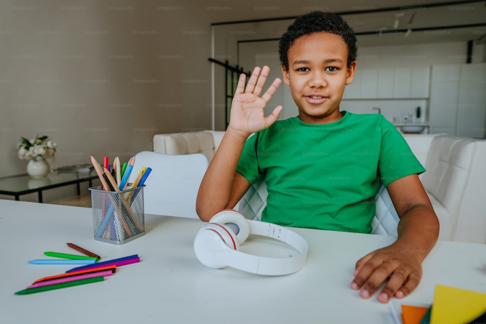 Portrait of a boy looking at camera waving hand and saying hello during online lesson at home.