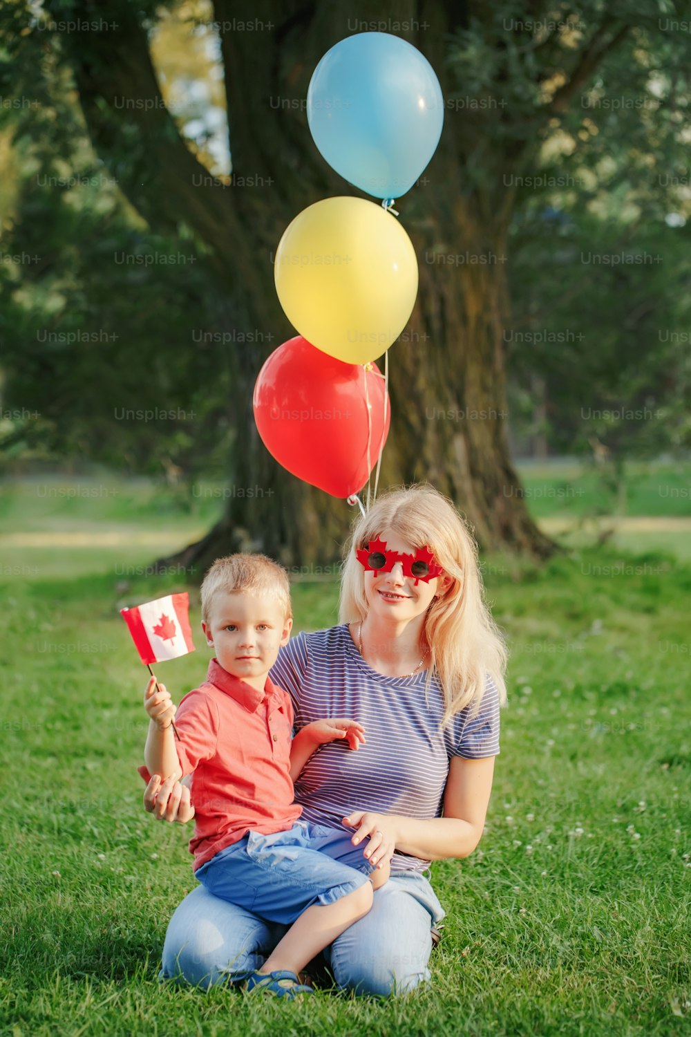 Mãe da família dos cidadãos com criança que celebra o Dia Nacional do Canadá em 1 de julho. Mãe caucasiana com bebê menino vestindo folha de bordo engraçada e óculos de sol de coração.