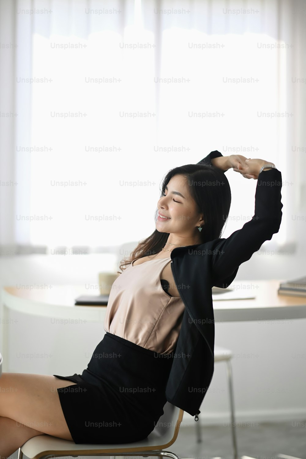 Portrait of young female office worker relaxing and stretching her body at workplace.